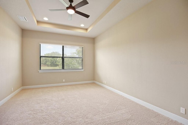 empty room with visible vents, light carpet, a ceiling fan, a tray ceiling, and baseboards