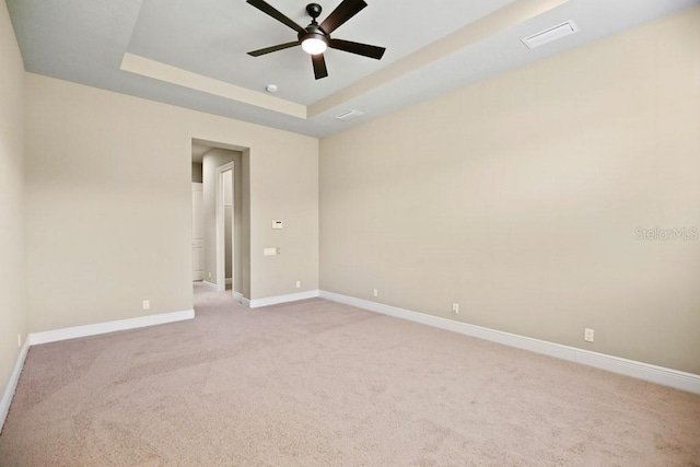 unfurnished room featuring a ceiling fan, baseboards, visible vents, a tray ceiling, and light colored carpet