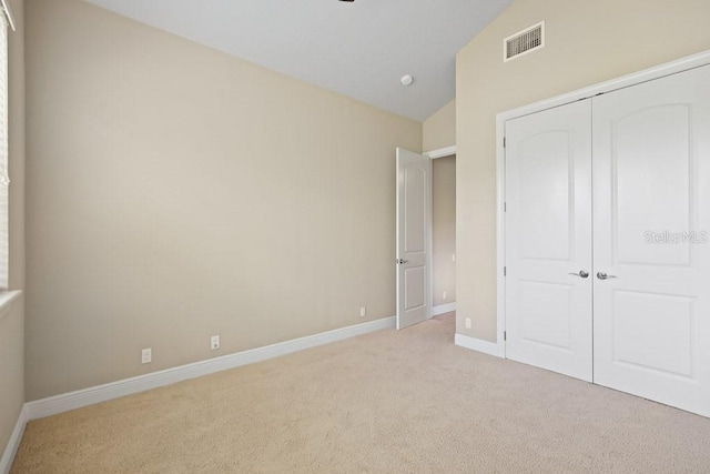 unfurnished bedroom with visible vents, light carpet, a closet, baseboards, and vaulted ceiling