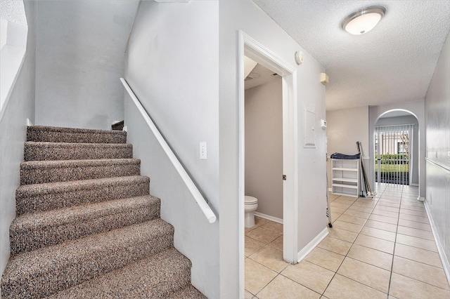 stairway featuring arched walkways, a textured ceiling, baseboards, and tile patterned floors