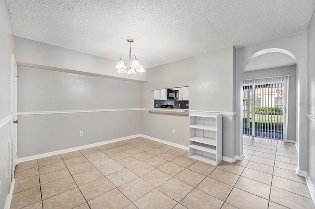 spare room featuring light tile patterned floors, a textured ceiling, arched walkways, a chandelier, and baseboards