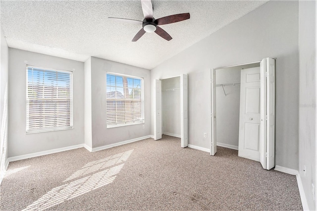 unfurnished bedroom with multiple closets, lofted ceiling, light colored carpet, a textured ceiling, and baseboards