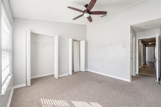 unfurnished bedroom with carpet floors, two closets, visible vents, vaulted ceiling, and a textured ceiling