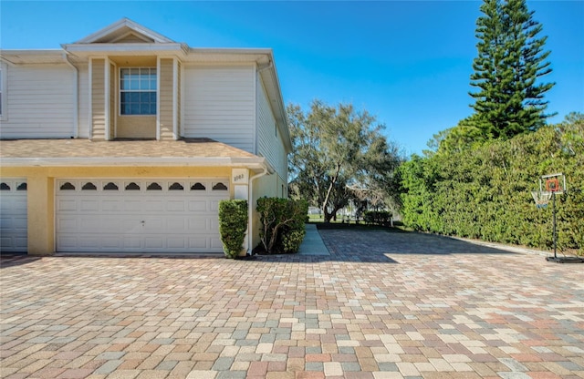 view of side of home with roof with shingles, decorative driveway, and an attached garage