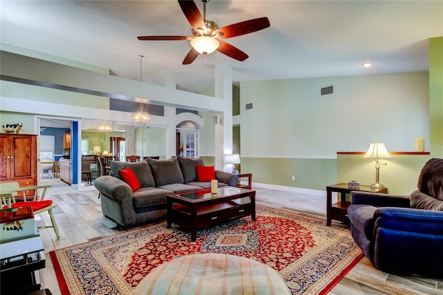 living area with lofted ceiling, visible vents, wood finished floors, baseboards, and ceiling fan with notable chandelier