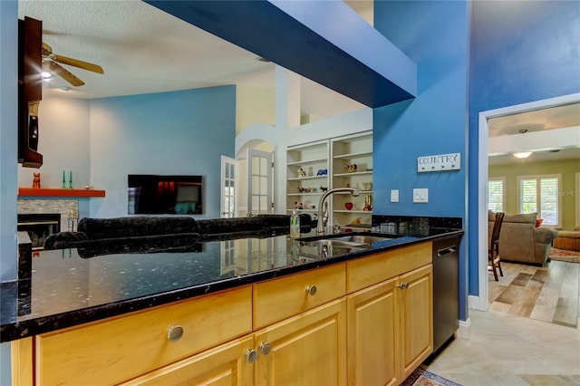 kitchen featuring a fireplace, open floor plan, a sink, dark stone counters, and dishwasher