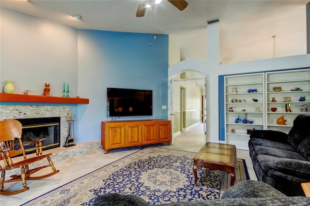 living room with arched walkways, a fireplace, a textured ceiling, and ceiling fan