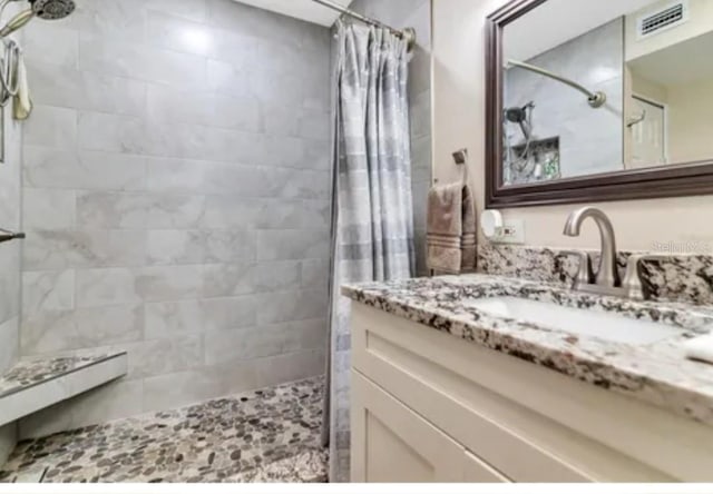 bathroom featuring visible vents, tiled shower, and vanity