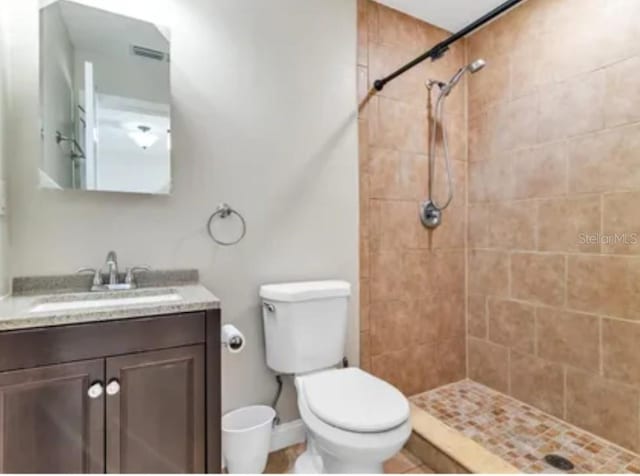 bathroom with toilet, tiled shower, vanity, and baseboards