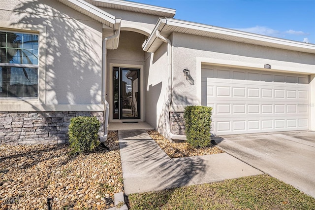 view of exterior entry with driveway, an attached garage, and stucco siding