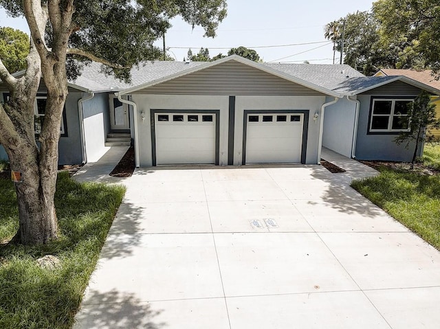 ranch-style home with an attached garage, a shingled roof, concrete driveway, and stucco siding