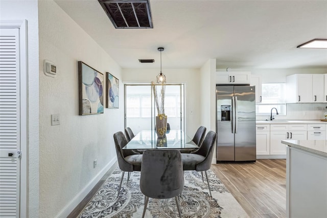 dining room featuring light wood-style floors, visible vents, a textured wall, and baseboards