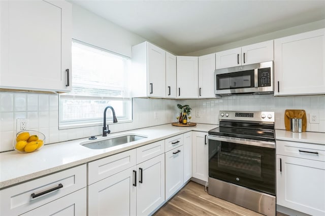 kitchen featuring decorative backsplash, stainless steel appliances, light wood-style floors, white cabinetry, and a sink