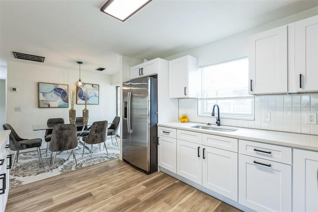 kitchen featuring decorative light fixtures, stainless steel refrigerator with ice dispenser, light countertops, white cabinets, and a sink