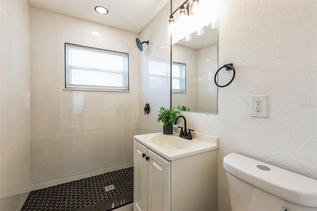 full bath featuring toilet, a textured wall, tiled shower, and vanity