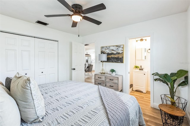 bedroom featuring visible vents, ensuite bath, light wood-style flooring, ceiling fan, and a closet