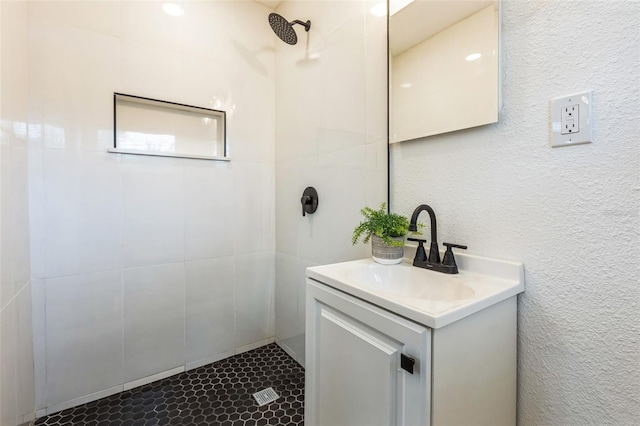 bathroom with a textured wall, a tile shower, and vanity