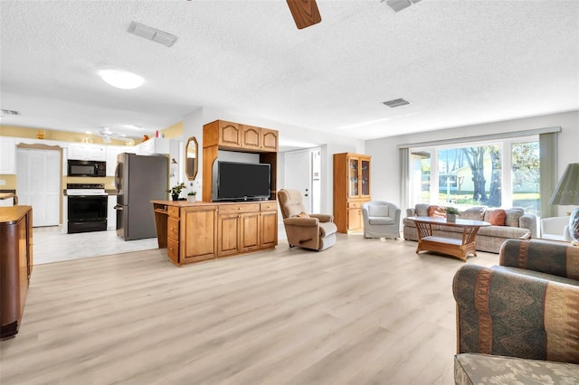 living area with visible vents, light wood-style floors, ceiling fan, and a textured ceiling