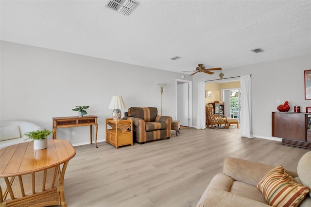 living area featuring visible vents, baseboards, a textured ceiling, and light wood-style flooring