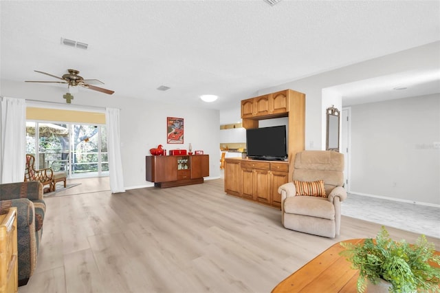 living area with visible vents, baseboards, a textured ceiling, and light wood-style flooring