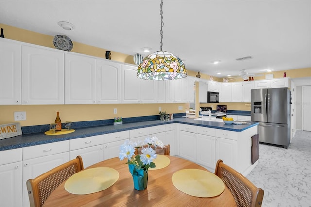 kitchen with dark countertops, black microwave, white cabinets, a peninsula, and stainless steel fridge