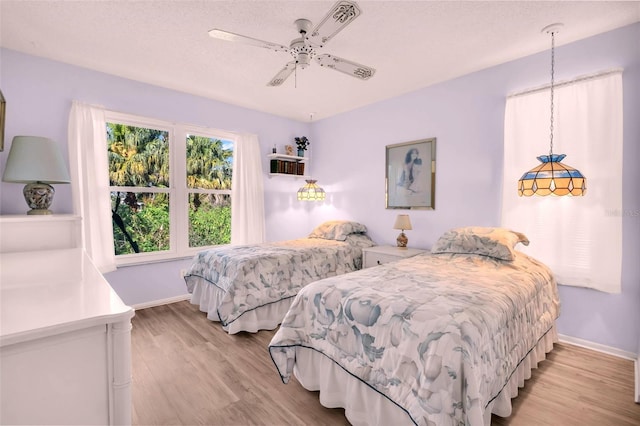 bedroom with a textured ceiling, baseboards, light wood-style floors, and a ceiling fan