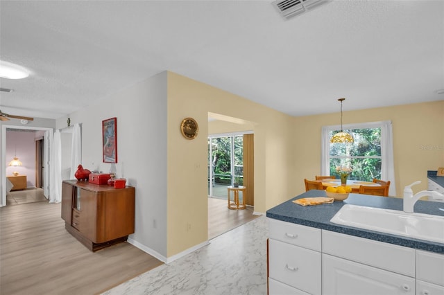 kitchen featuring hanging light fixtures, white cabinets, visible vents, and a sink