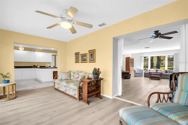 living area with visible vents, baseboards, a ceiling fan, and light wood finished floors