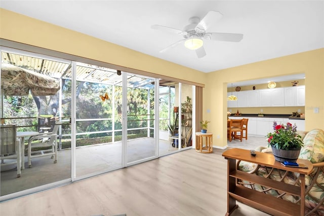 doorway with light wood-style flooring, baseboards, and ceiling fan