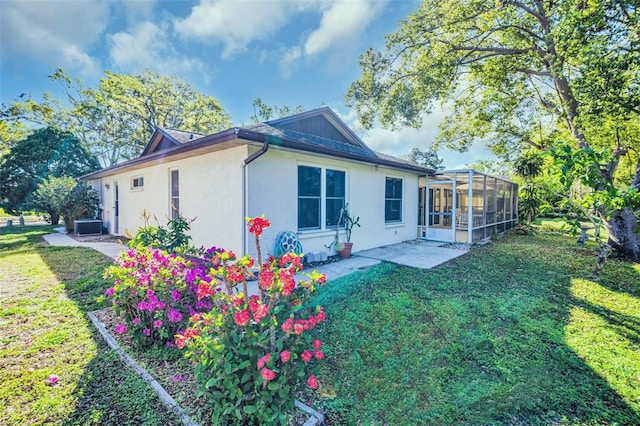 rear view of property with stucco siding, a lanai, central air condition unit, a patio area, and a lawn