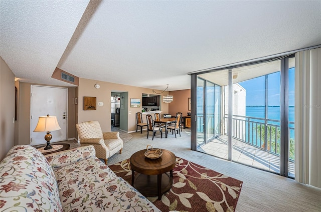 living room with a textured ceiling, a wall of windows, and light colored carpet