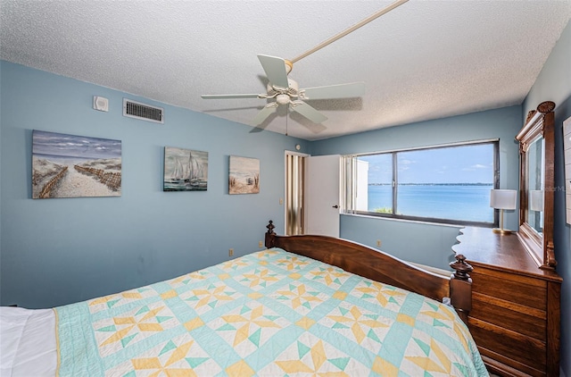 bedroom featuring a textured ceiling, a water view, visible vents, and a ceiling fan