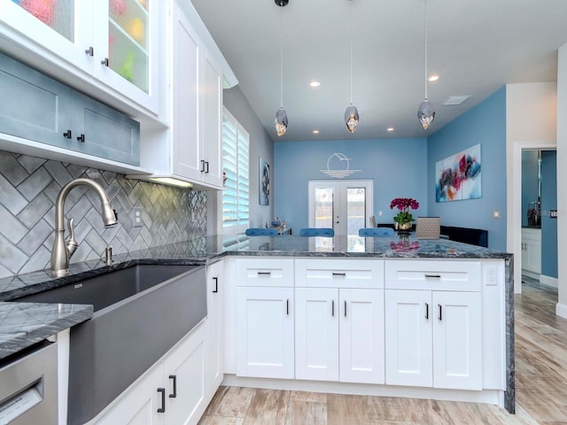 kitchen featuring a peninsula, a sink, white cabinets, french doors, and dark stone counters