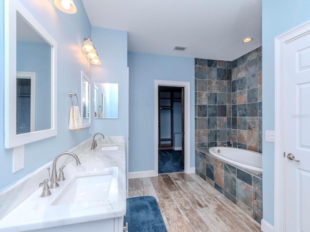 bathroom featuring double vanity, tiled bath, a sink, and wood finished floors