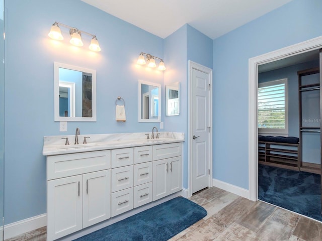 bathroom with double vanity, wood finished floors, a sink, and baseboards