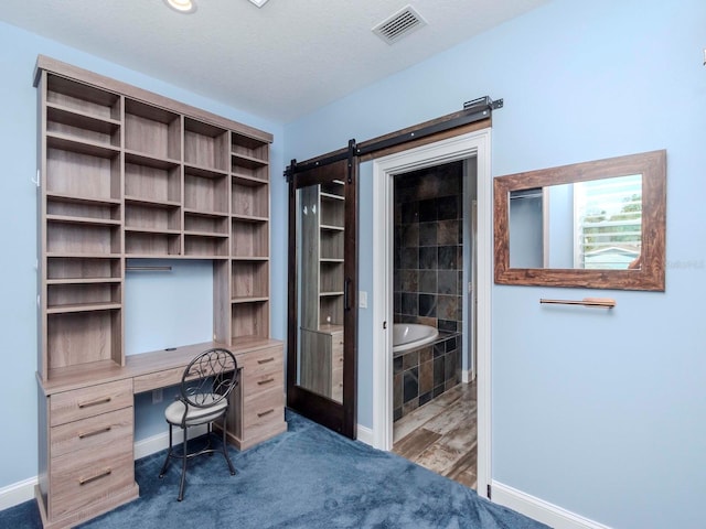 unfurnished office with visible vents, a textured ceiling, baseboards, and a barn door