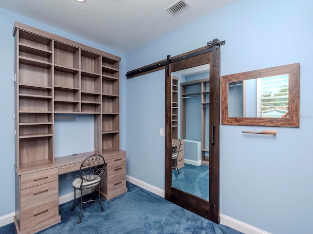 unfurnished office featuring a textured ceiling, a barn door, visible vents, baseboards, and dark colored carpet