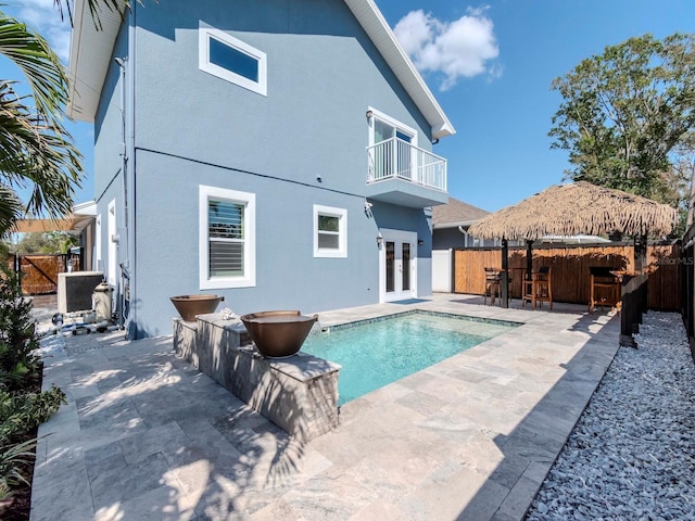 rear view of property featuring french doors, a patio, stucco siding, a balcony, and a fenced backyard