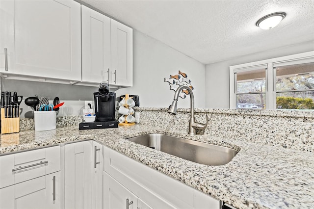 kitchen featuring white cabinetry, a sink, a textured ceiling, and light stone countertops