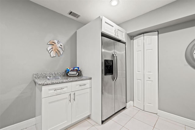 kitchen with light tile patterned floors, light stone counters, visible vents, white cabinets, and stainless steel fridge