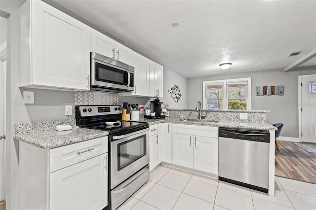 kitchen with a peninsula, a sink, visible vents, white cabinets, and appliances with stainless steel finishes