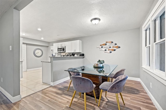 dining room featuring a textured ceiling, light wood finished floors, and baseboards