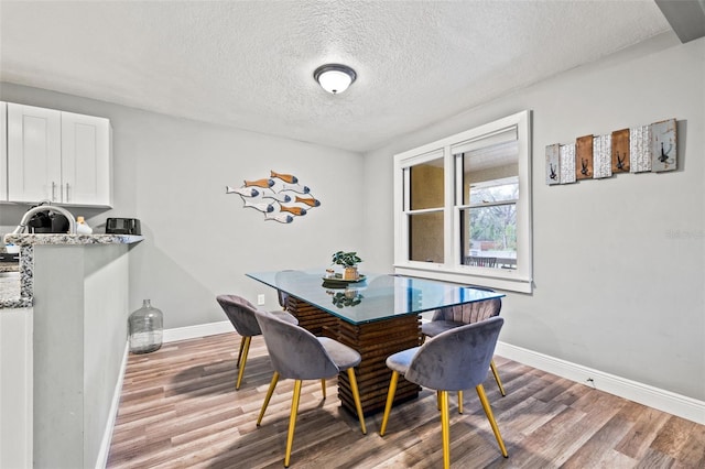 dining space with baseboards, a textured ceiling, and light wood-style floors