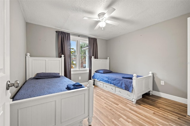 bedroom with a ceiling fan, a textured ceiling, baseboards, and wood finished floors