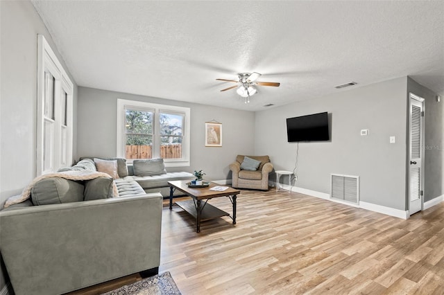 living room with a textured ceiling, light wood-type flooring, visible vents, and baseboards