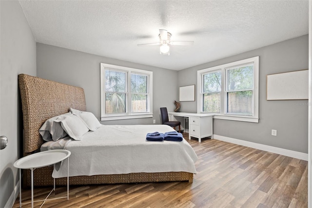 bedroom featuring ceiling fan, multiple windows, baseboards, and wood finished floors