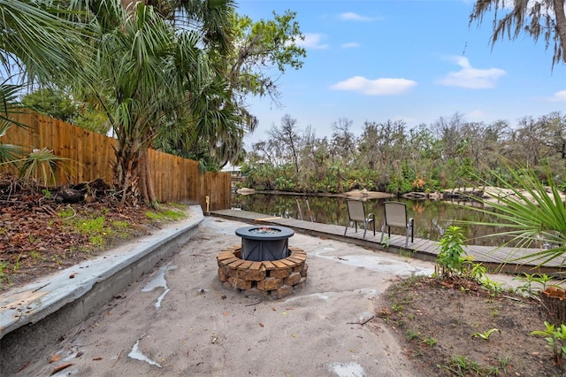 view of patio featuring a water view, a dock, fence, and a fire pit