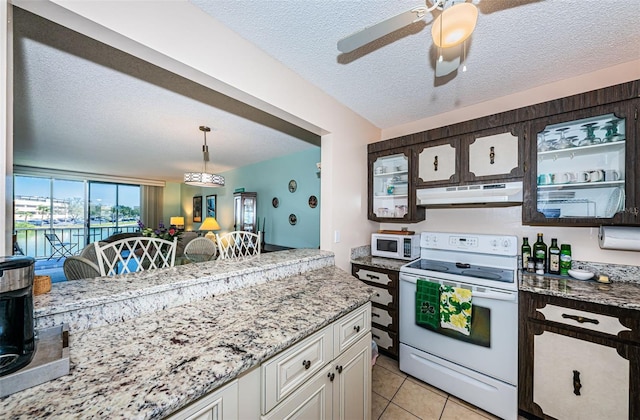 kitchen with white appliances, light tile patterned floors, light stone countertops, a textured ceiling, and under cabinet range hood