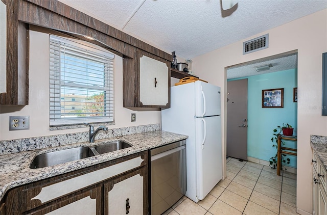 kitchen with a textured ceiling, a sink, visible vents, stainless steel dishwasher, and freestanding refrigerator