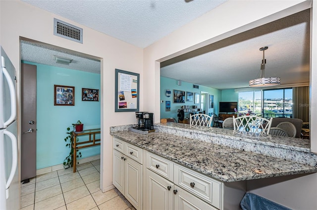 kitchen with a textured ceiling, light stone counters, a peninsula, visible vents, and fridge